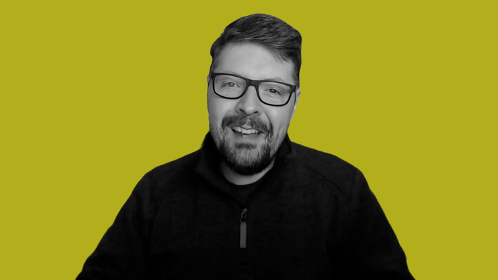 Paul Kilduff-Taylor smiles at the camera. He is grayscale in front of a grokludo yellow background.