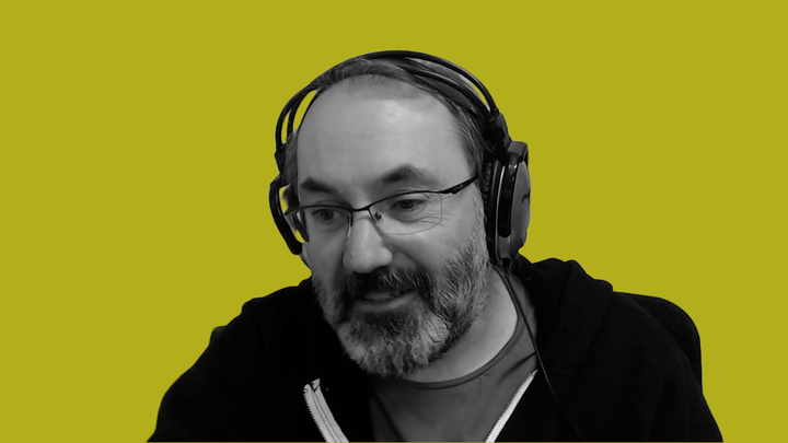 José Zagal in black and white, smiling at his computer screen, in front of a grokludo yellow background.